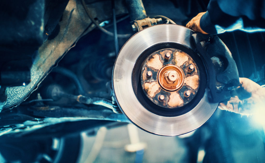 Closeup of a mechanic replacing car brake pads. The car is lifted with hydraulic jack at eye level.