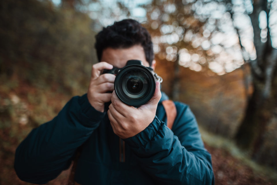 Young man using a DSLR camera in a forest in autumn