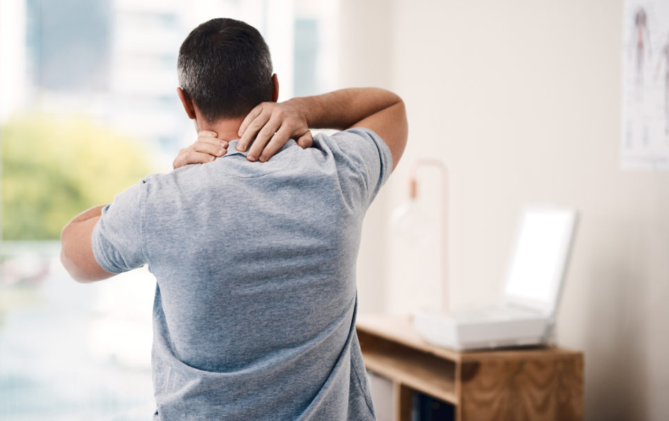 Rearview shot of an unrecognizable male patient holding his neck while standing in his office