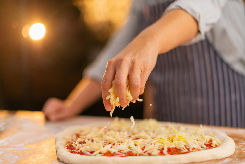 Man sprinkling cheese on pizza