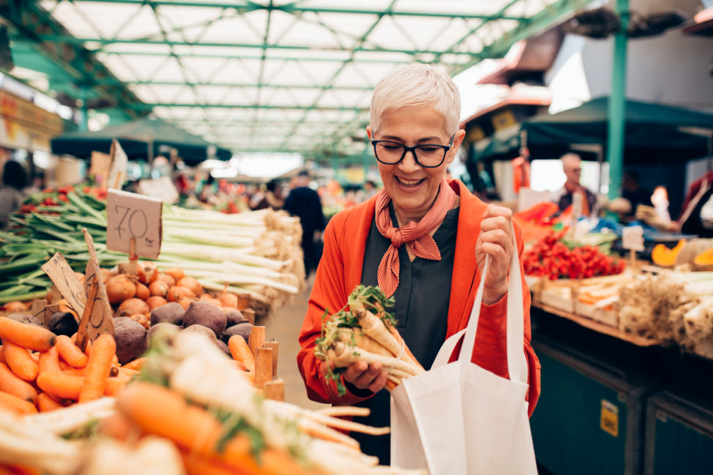 One elderly woman buying a bundle of carrots at a community marketplace