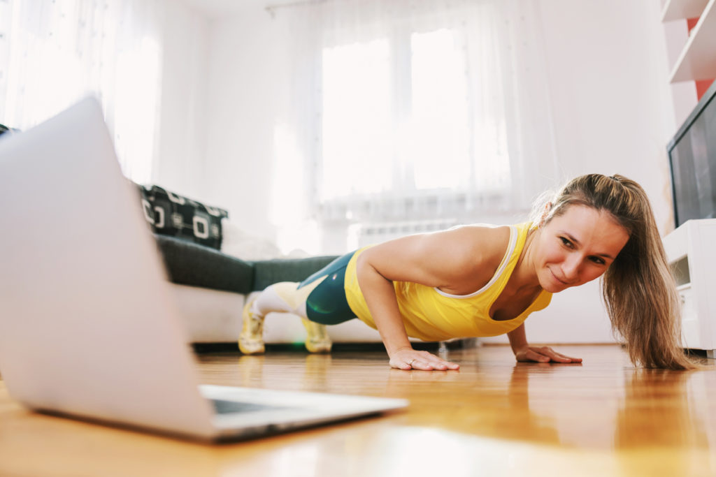 Fitness instructor doing pushups at home and having online class with her students.