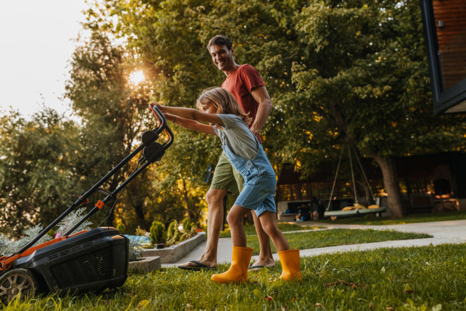 Father and his little son mowing the lawn together at home