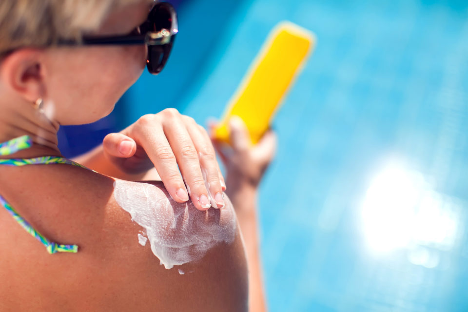 Woman applies sun protection cream on her skin. People, summer, vacation and healthcare concept